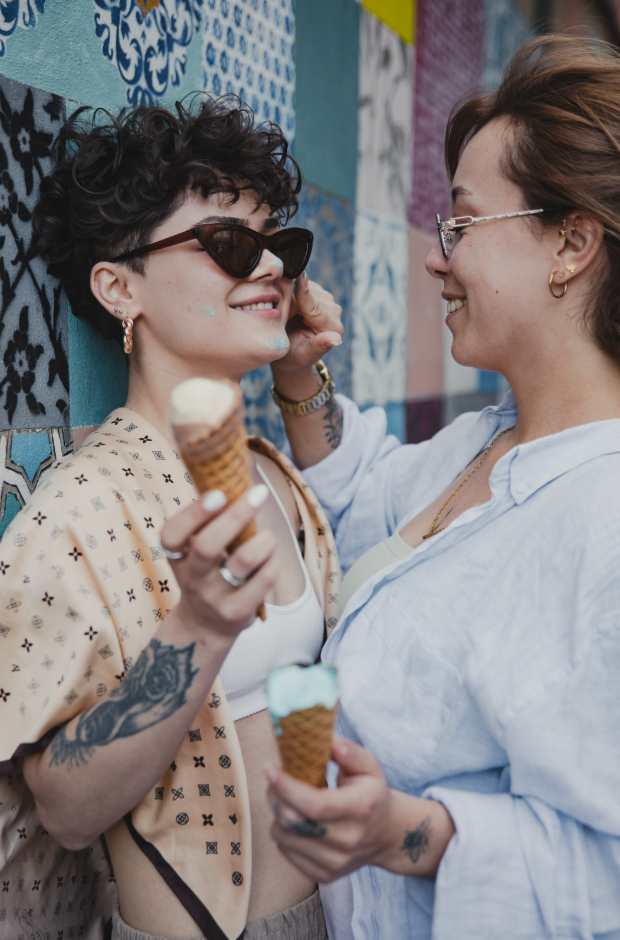 Two women smiling at each other over ice cream cones in front of a colorful tiled wall